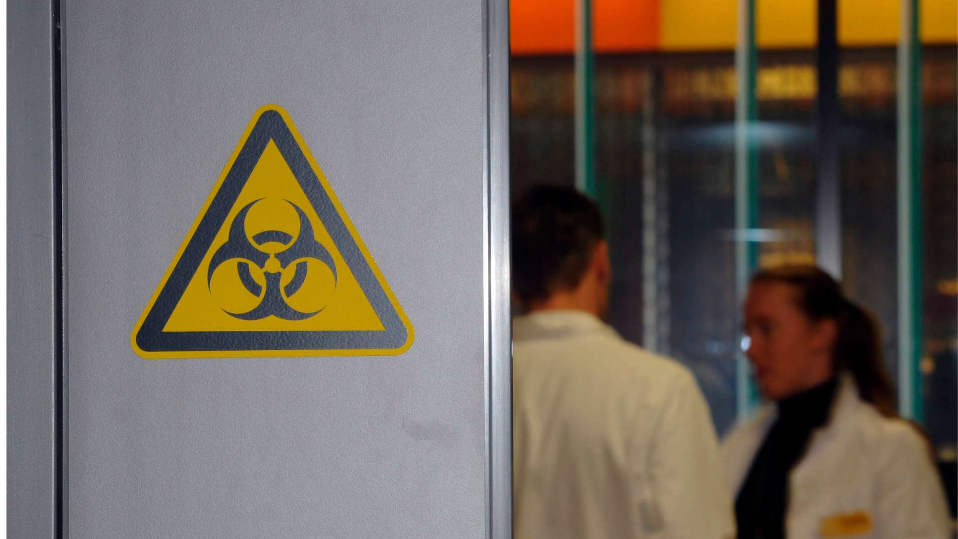 Tecnici di laboratorio dietro ad una porta con il logo del rischio biologico