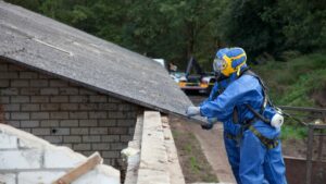 Operatori che con tuta e maschera che rimiovo un tetto con amianto