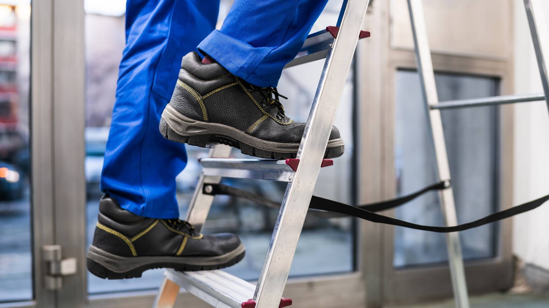 Uomo che sale su una scala portatile. Ha scarpe antinfortunische e tuta da lavoro blu